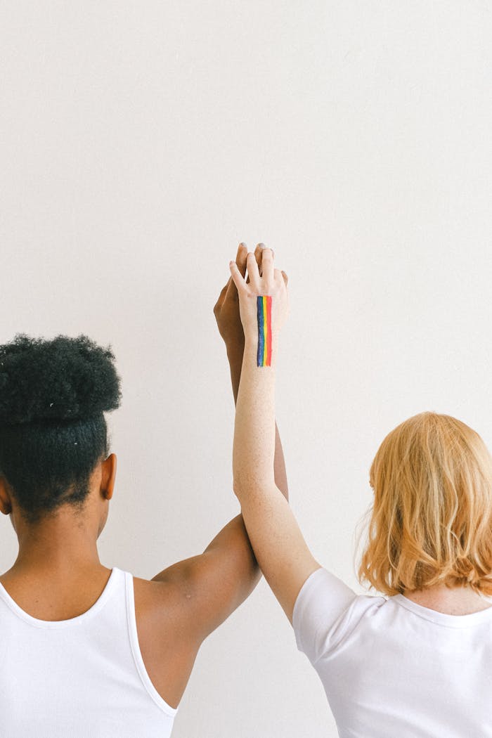 An interracial couple showing unity and pride with raised arms and a rainbow tattoo.
