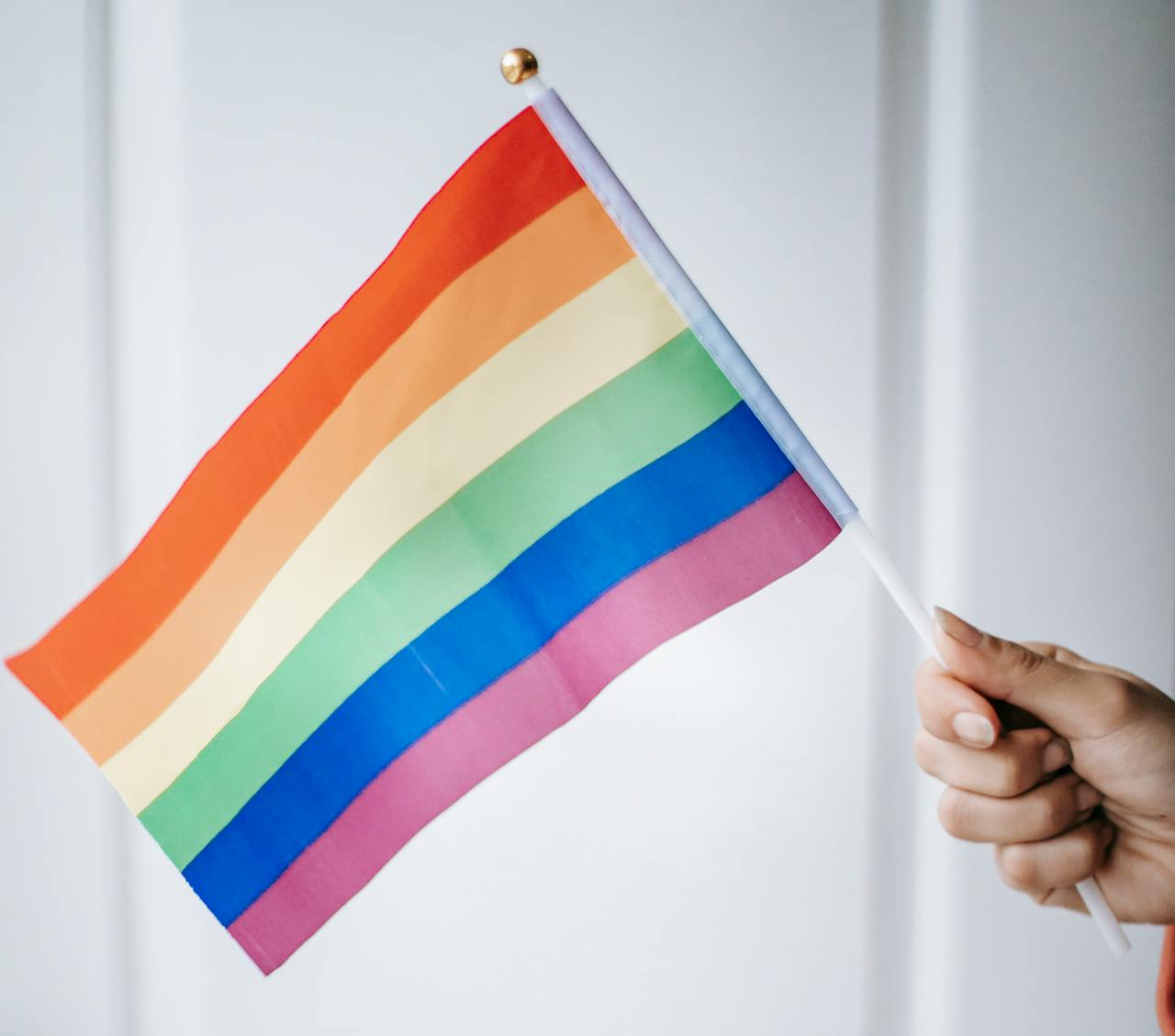 A colorful rainbow flag representing LGBTQ pride being held indoors, symbolizing freedom and diversity.