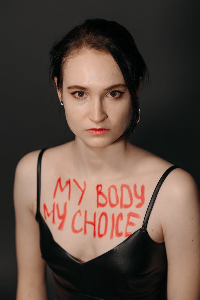 A serious woman with 'My Body My Choice' painted on her chest, emphasizing empowerment.